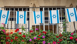 String of Israeli flags on fence with flowers